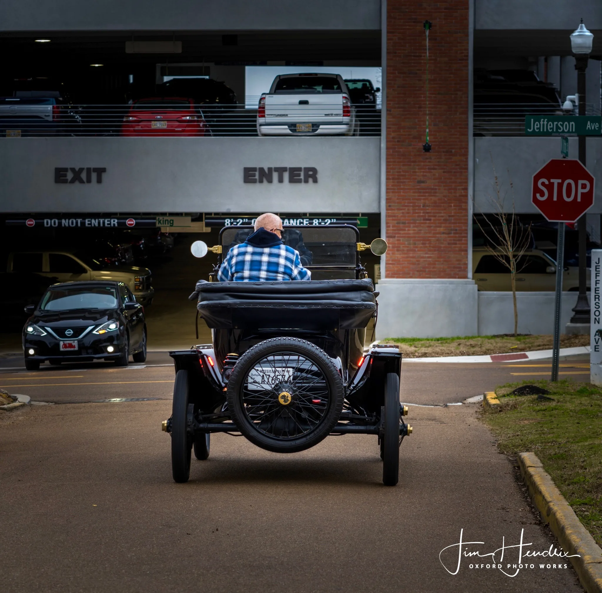 Rear view of man driving antique black car toward parking garage entrance at Jefferson Avenue.