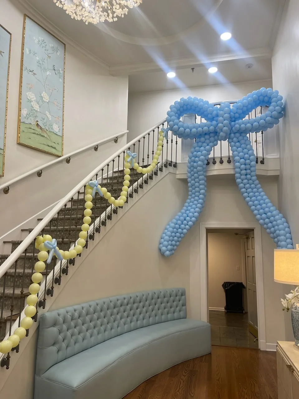 Large light blue balloon bow with yellow balloon garland on an indoor staircase.