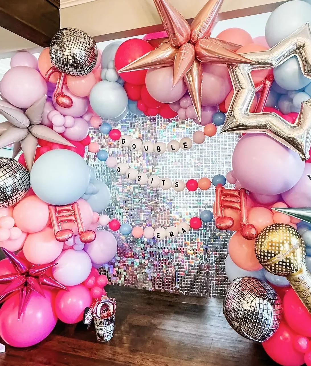 Colorful balloon backdrop with disco balls, stars, and “Double Digits Era” banner in front of a sequin wall.
