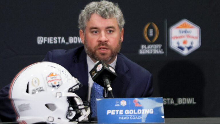 Ole Miss Rebels coach Pete Golding on the stage at a press conference with Miami Hurricanes coach Mario Cristobal