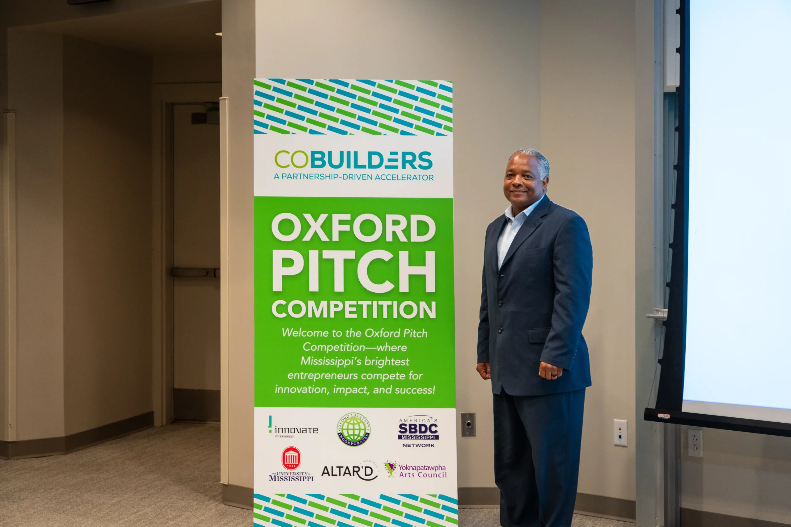 American Drone Solutions representative stands beside the CoBuilders Oxford Pitch Competition sign.